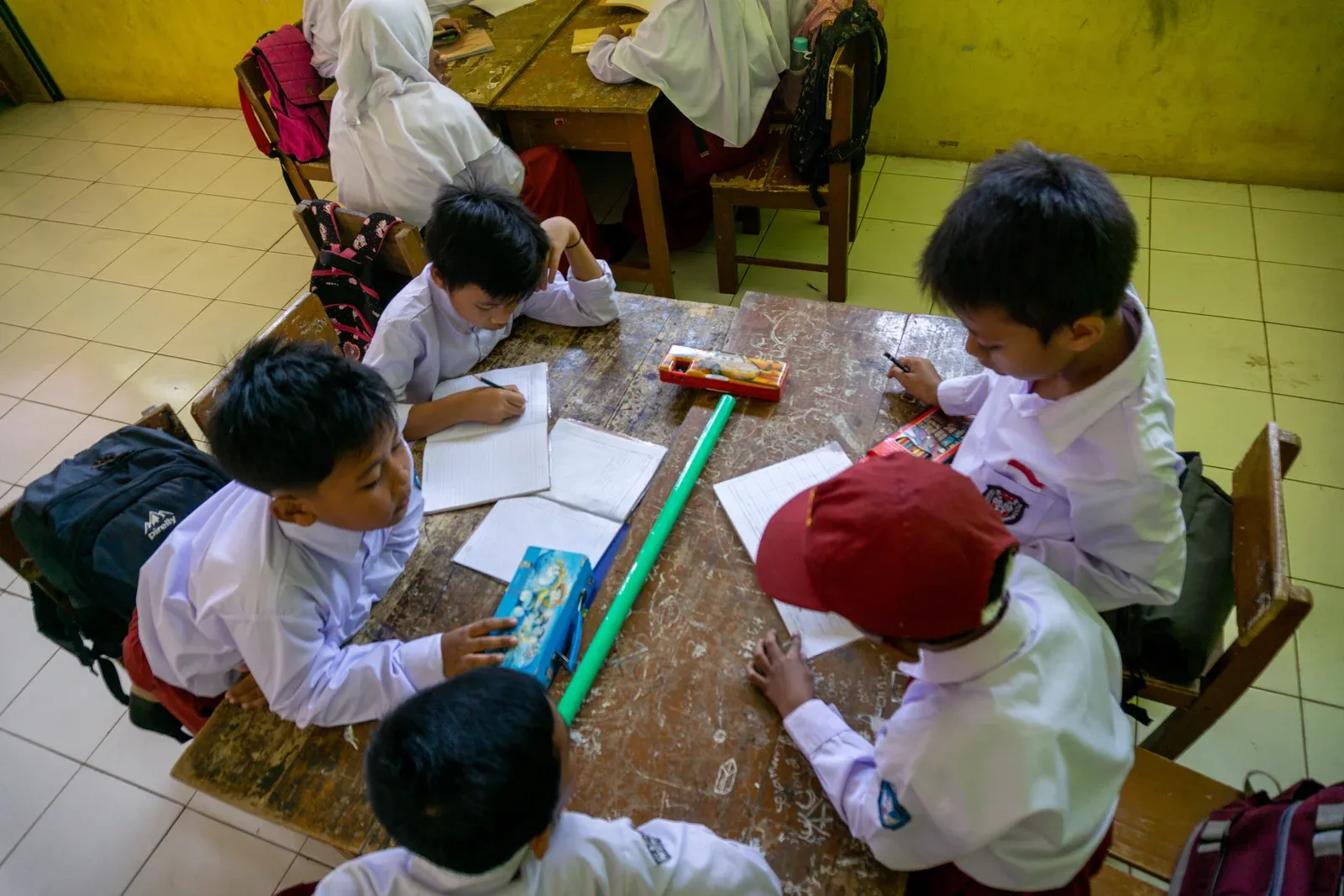 Anak-anak belajar bersama di meja kelas, difoto dari atas.